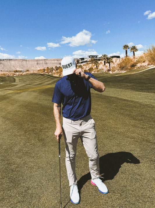Golfer on fairway wearing white classic Country Club GUEST golf hat and holding club