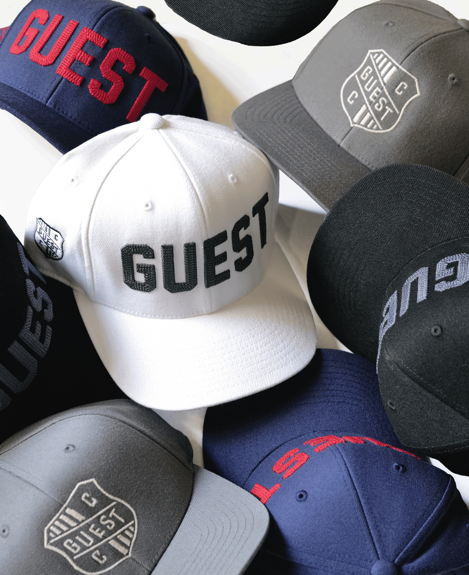 Collection of Guest golf hats displayed in a flat lay arrangement, showing multiple colors and embroidered designs