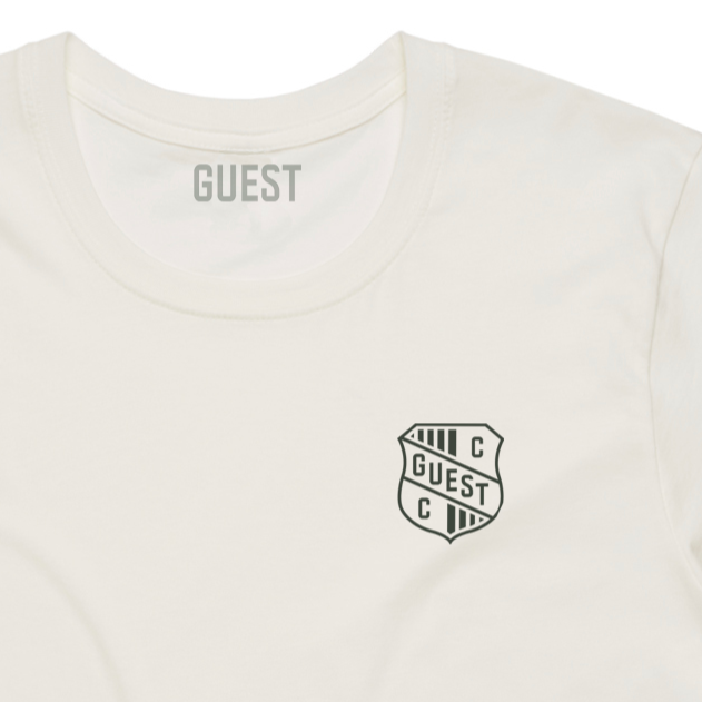 Close-up of Natural Country Club GUEST t-shirt featuring small crest logo on left chest