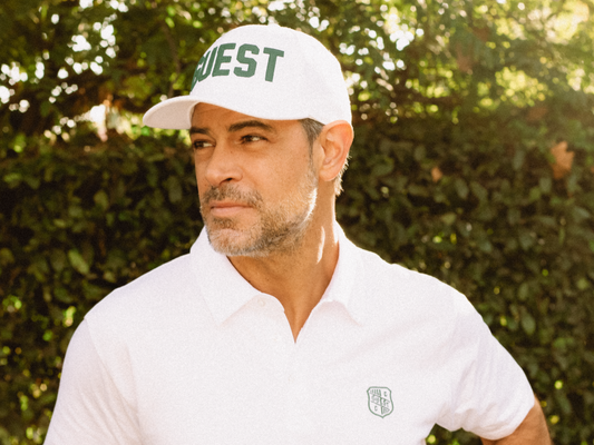 Man wearing a white Country Club Guest golf hat and white embroidered polo shirt outdoors