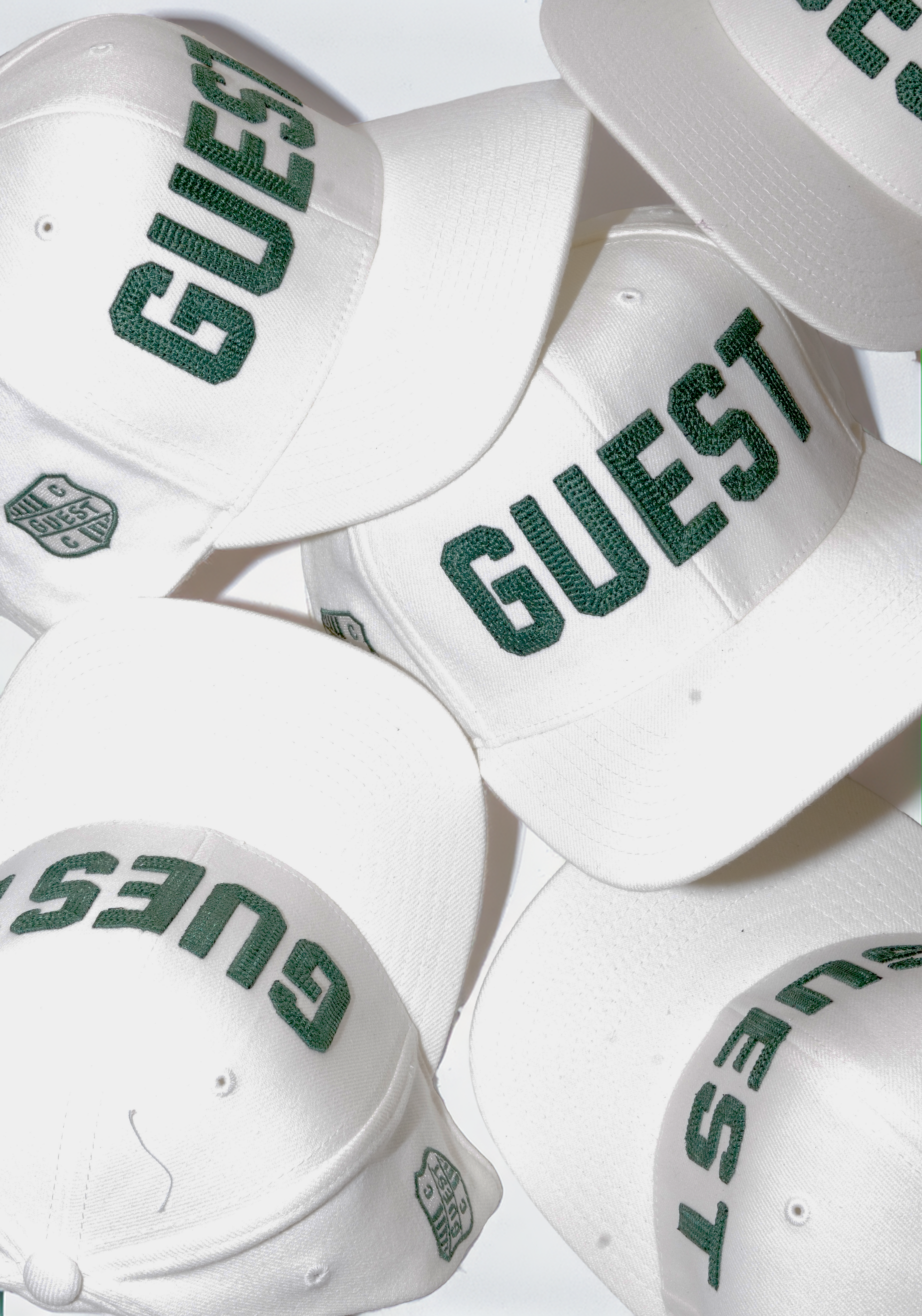 Flat lay of classic white Country Club Guest golf hats with green embroidered lettering and crest