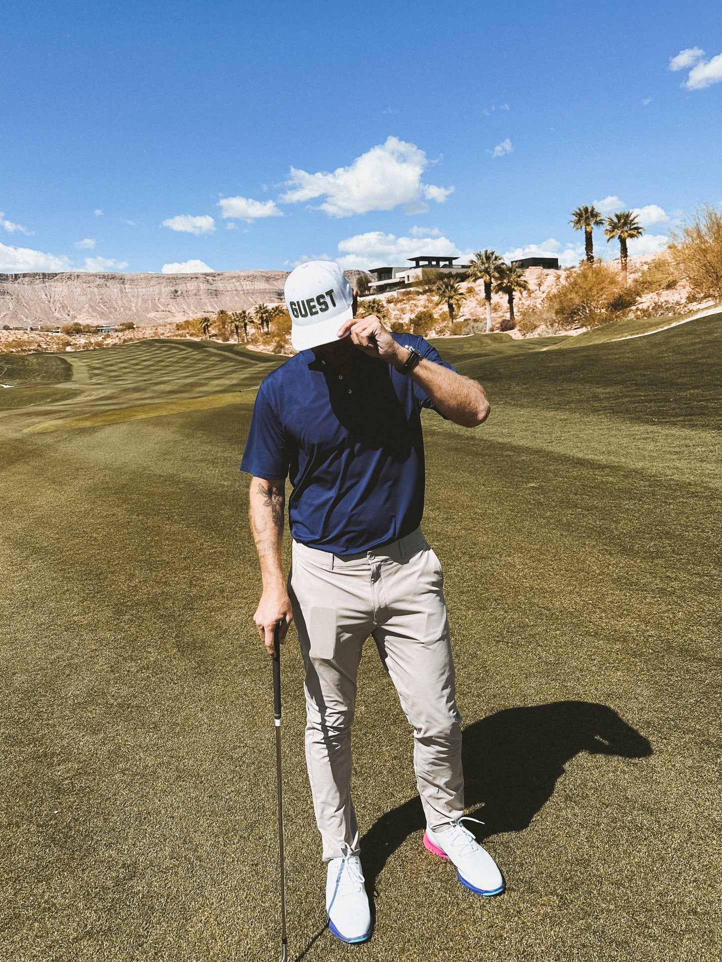 Golfer on fairway wearing white classic Country Club GUEST golf hat and holding club