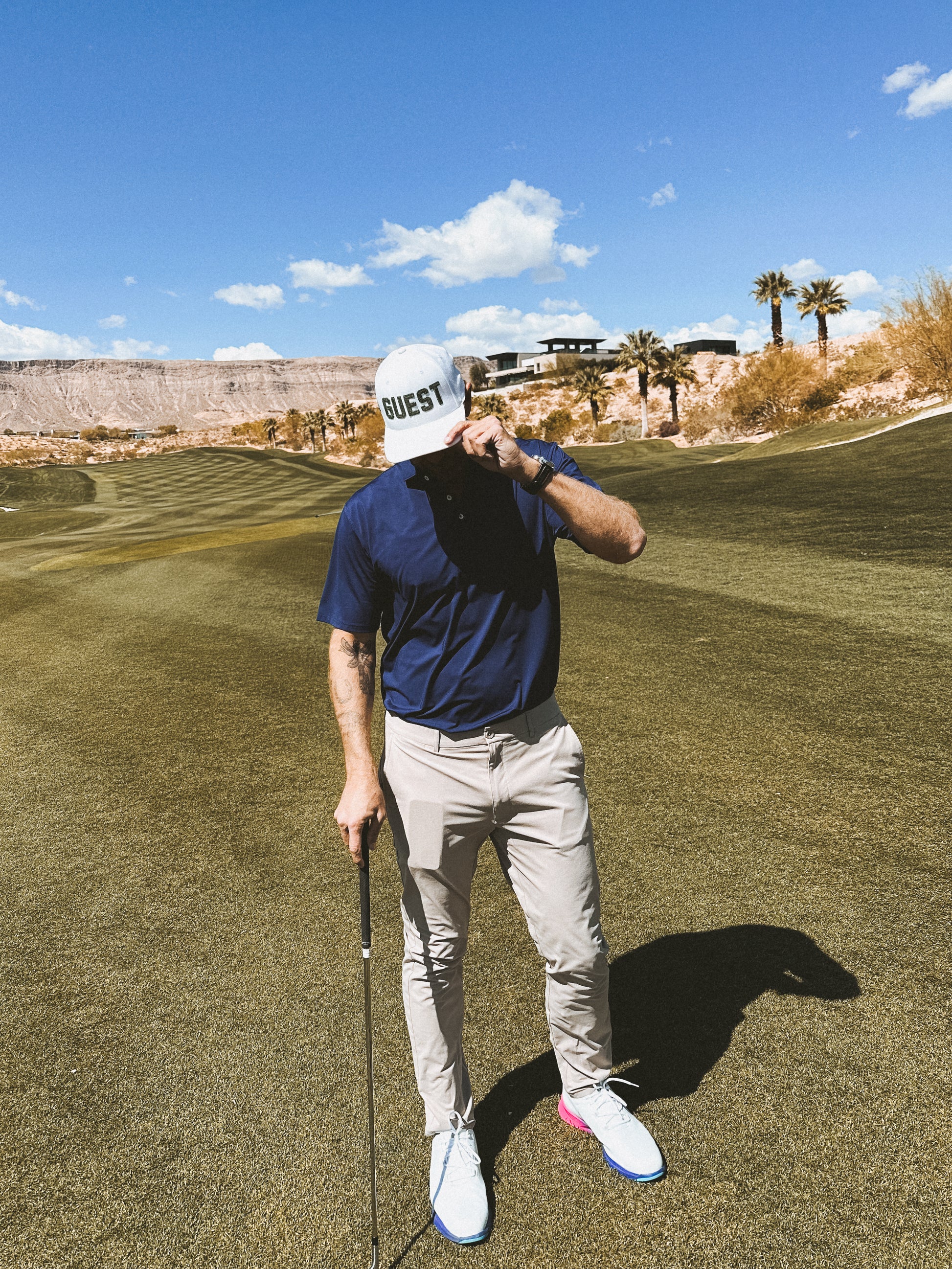 Golfer on fairway wearing white classic Country Club GUEST golf hat and holding club